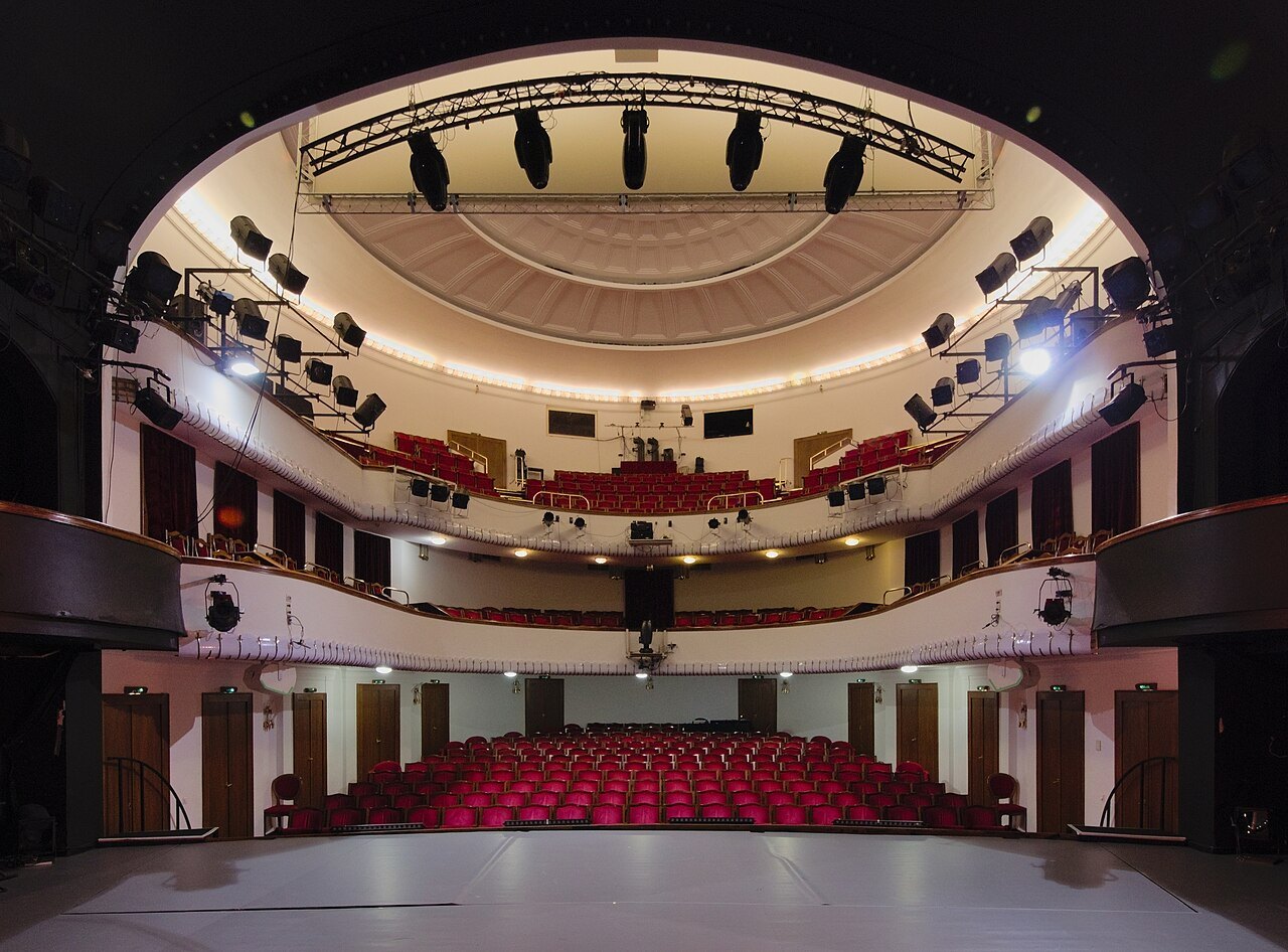 Theatre auditorium with balconies, seating rows and stage lighting.