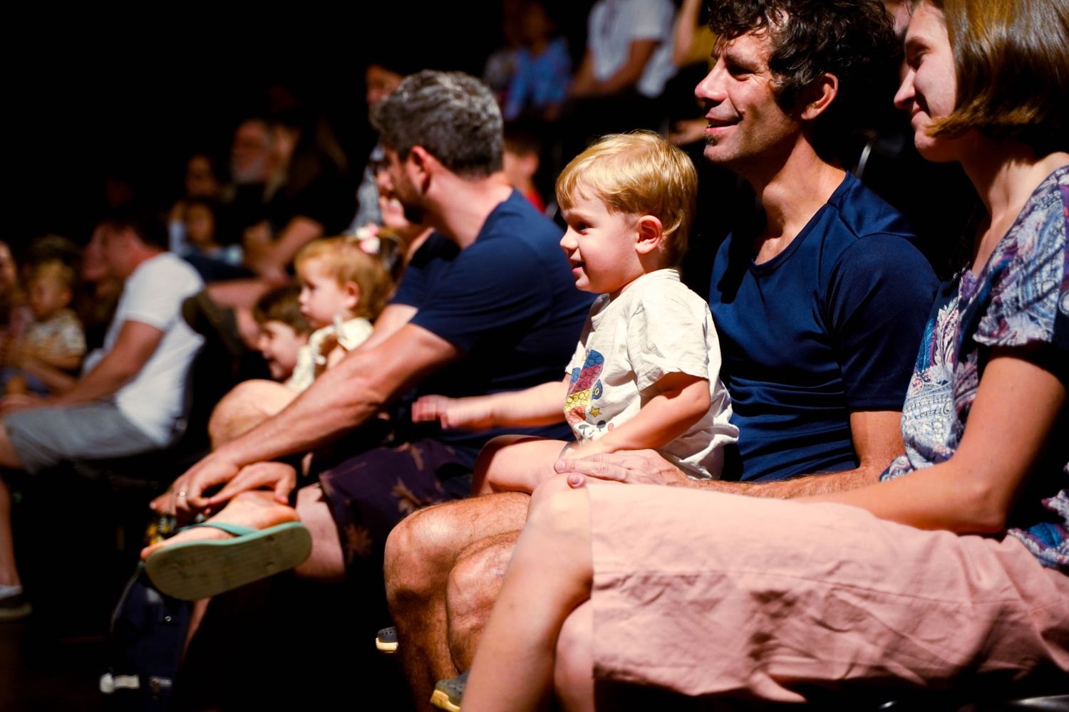 Children and adults sit together in the audience at a performance.