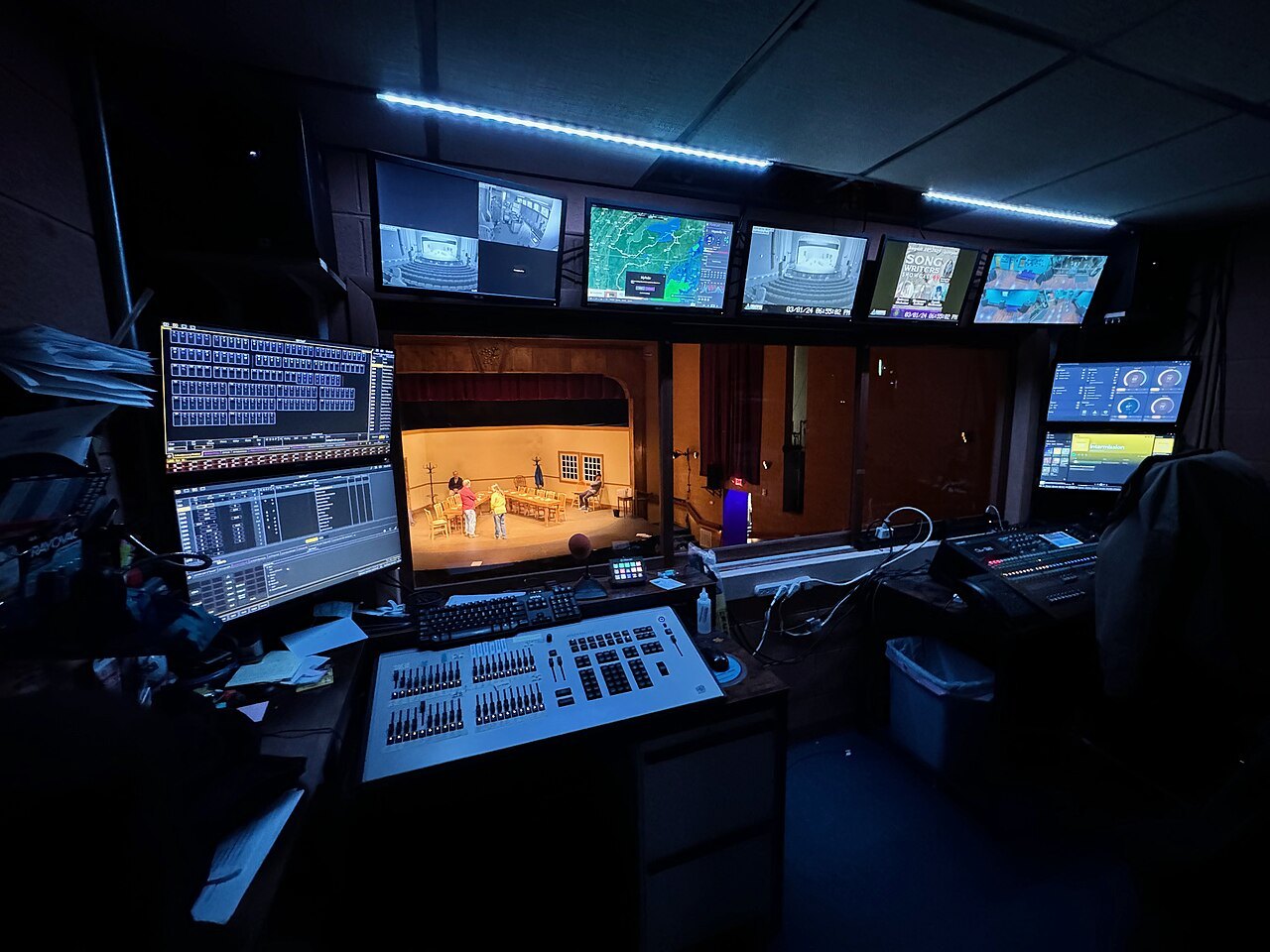Technical control room with consoles and a view of a theatre stage.